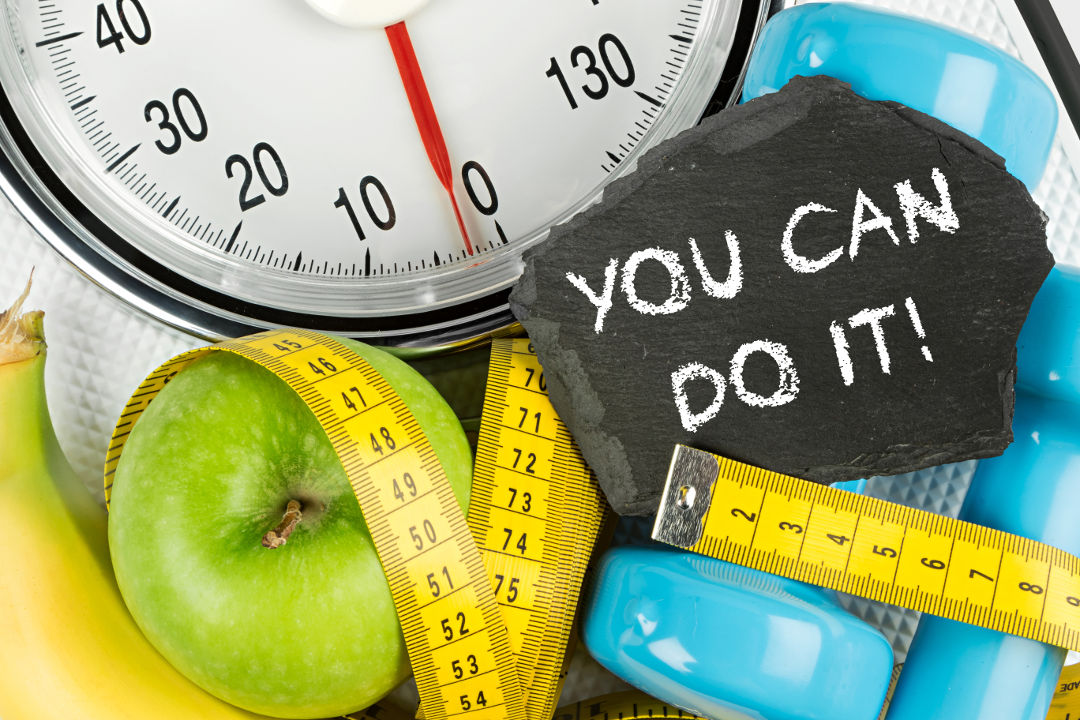 Alles, was du zum Thema abnehmen wissen solltest Abnehm-Waage mit Maßband, Handteln und Obst sowie eine Tafel mit Schriftzug: YOU CAN DO IT!